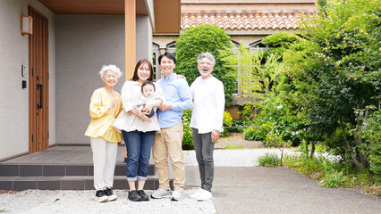 住宅の前で笑顔で赤ちゃんを囲む三世代家族