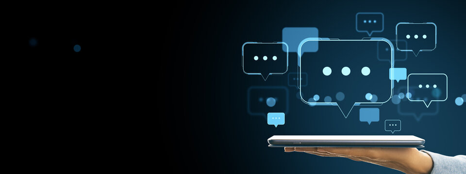 Digital chat communication concept with speech bubbles floating above a tablet device held by a hand on a dark background.