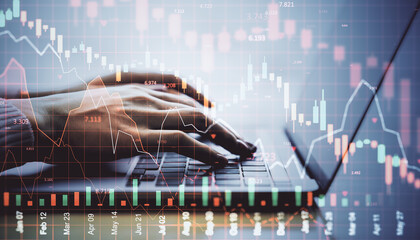Hands typing on laptop with falling stock market chart overlay, symbolizing financial crisis, investment loss, and global economic downturn.