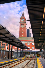 View of Seattle's historic King Street Station under a dramatic sky, showcasing its iconic clock tower rising above train tracks and platform roofs