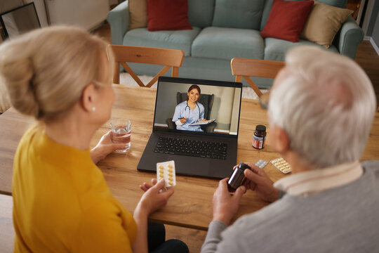 At a dining room table, a senior couple uses a laptop to video conference with a Doctor about their various medications. The couple are receiving home health care and advice virtually. - Powered by Adobe