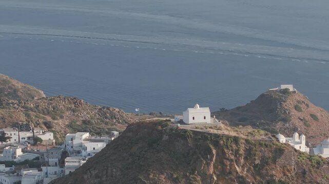 Orbit zoom aerial view of Plaka castle in Milos Greece, with ship sailing in the background. 3x telephoto, D-Log M profile