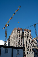 Tower cranes operating at a busy construction site, erecting a modern apartment building beneath a...