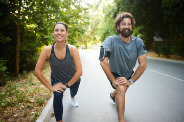 Two individuals are engaged in a joyful workout, performing lunges on a tree-lined road during a...