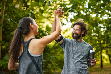 Two individuals happily high-five each other after completing their workout in a tranquil park, showcasing the joy of exercising in nature and fostering healthy habits among friends.