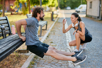 Two individuals are active in a community park, performing exercises. A man is doing dips on a...