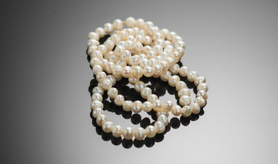 Pearl necklace over black background, close up. Beautiful Natural pearls beads, elegant accessories macro shot. Pearl gemstones, glamour. Top view. 