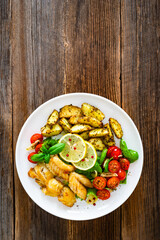 Seared pollock fish, baked potato wedges and tomato salad on wooden table	