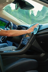 Close-up of male hand wiping car dashboard with microfiber cloth for cleaning. Concept of vehicle hygiene, interior maintenance and car detailing