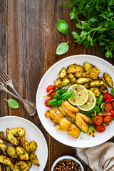 Seared pollock fish, baked potato wedges and tomato salad on wooden table	