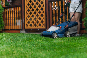 This image captures someone mowing their lawn with a push lawn mower. The person is holding onto...