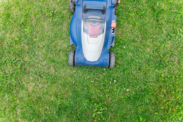 Lawn mower cutting green grass in backyard. Gardening background.