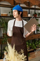 Handsome young man tending to plants and engaging with technology in a cozy studio environment
