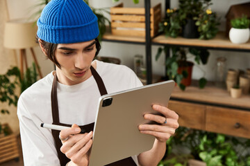 Handsome young man carefully tending to plants while using a tablet in a bright studio space