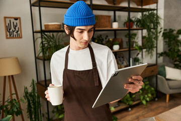Young man tending to plants in modern studio while enjoying a warm beverage and digital planning