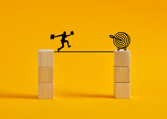 Businessman running on a tightrope between two stacks of blocks towards target