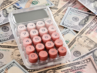 Pink calculator lying on United States one hundred dollar bills calculating income