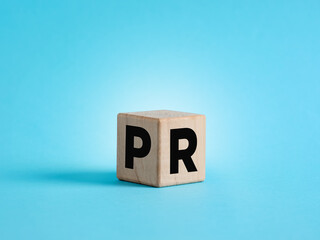 Wooden cube showing acronym PR, public relations, on blue background