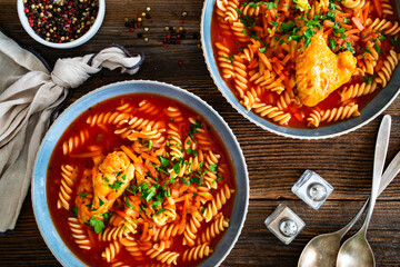 Tomato soup with chicken thigh and noodles on wooden table