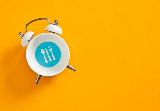 White alarm clock with cutlery icons showing lunch time on orange background