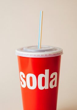 Red soda cup with "soda" written on it and a straw, on a light background