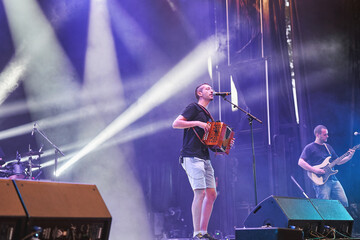 Live stage performance with male accordion and electric guitar players under colorful lights