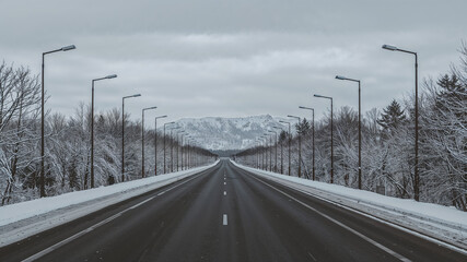 Empty asphalt road leading to snowy mountain in winter