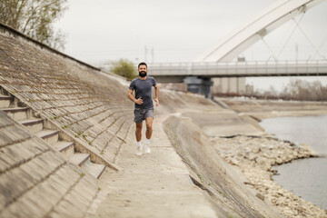 Full length of sportsman in shape running towards camera near riverside.
