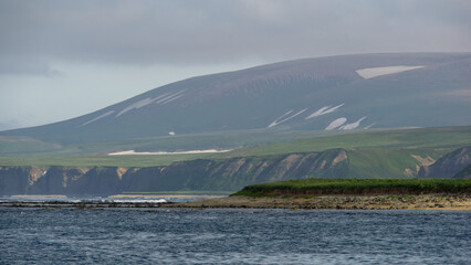 Serene coastal landscape featuring rolling green hills and cliffs, with gentle waves lapping at the shore, creating a tranquil atmosphere in a natural environment