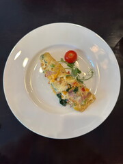 Colorful vegetable and ham omelette served with cherry tomato and greens on a white plate. High-end breakfast or brunch concept, perfect for menus or food ads.