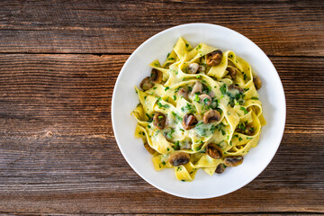 Papperdelle pasta with champignons mushrooms in cream sauce and parsley on wooden table	