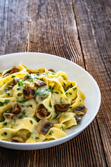 Papperdelle pasta with champignons mushrooms in cream sauce and parsley on wooden table	