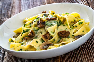 Papperdelle pasta with champignons mushrooms in cream sauce and parsley on wooden table	