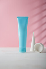Cosmetics blue tube template, blank mockup, no brand or logo. Concrete decor on pink background. Product presentation, advertising banner. Copy space