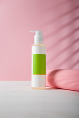 Cosmetics dispenser bottle with green blank template sticker, mockup, no brand or logo. Paper roll on pink background. Product presentation. Copy space