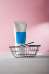 White blue cosmetics tube template, no brand container in shopping basket on pink background. Online beauty product order concept. Copy space