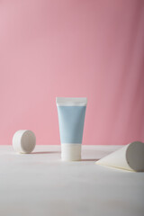 Tender blue cosmetics tube, concrete decor on pink background. Blank label, no brand logo template, mockup. Copy space. Product advertising banner