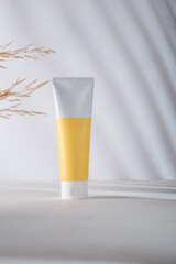 Unbranded Cosmetics tube with blank yellow label, mockup. Plant branch on white background. Beauty product template, advertising. Copy space.