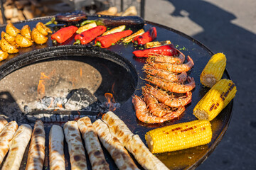 Variety of food being cooked on a grill. The food includes shrimp, corn on the cob, and flatbreads,...