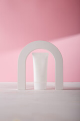 White cosmetics tube mockup template, concrete decorative arch on pink background. Unbranded beauty product in harsh light with shadows, no label. Copy space
