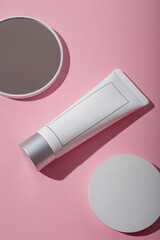 White unbranded cosmetics tube mockup, concrete stand and mirror on pink background. Beauty product template, advertising banner. Copy space. Flay lay, top view
