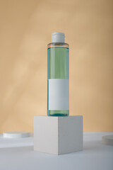 Transparent Cosmetics bottle with blue liquid, mockup on concrete cube stand, yellow background. Unbranded beauty container, no label template. copy space