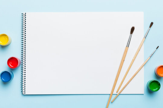 Album pages and paints, pencils, brush on a colored background. Top view with empty space. workplace for creativity. home teaching concept drawing
