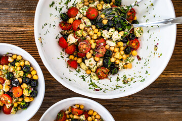 Fresh vegetable salad with chickpea, sliced chicken breast and cherry tomatoes on wooden table	