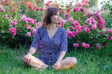 Beautiful young woman in a polka dot dress with roses, in a park on a sunny day