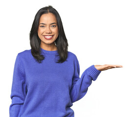 Simple portrait of a young Latina showing a copy space on a palm and holding another hand on waist.