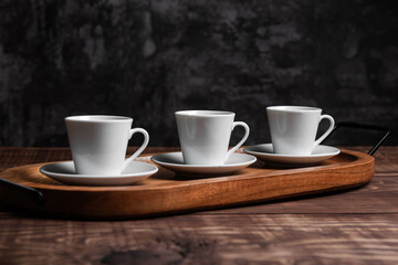 Three white espresso cups rest on matching saucers, arranged neatly on a rustic wooden serving tray