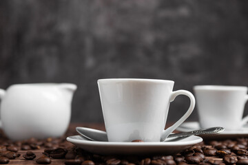 A white espresso cup and saucer nestled amongst dark roasted coffee beans.