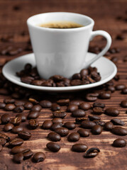 A espresso cup with dark coffee sits on a saucer, surrounded by roasted beans on a wooden surface.