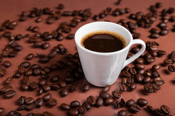 A espresso cup filled with dark coffee surrounded by roasted beans on reflective surface.
